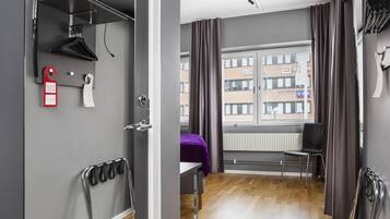 A modern hotel room with a wooden floor, a large window with curtains, a bed, a chair, and a radiator.