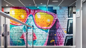 Un interno moderno con un murale colorato al muro, una porta in vetro e un corrimano in metallo.