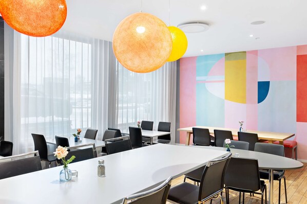 Una sala de conferencias moderna con mesas redondas, sillas negras y colorida decoración mural geométrica.