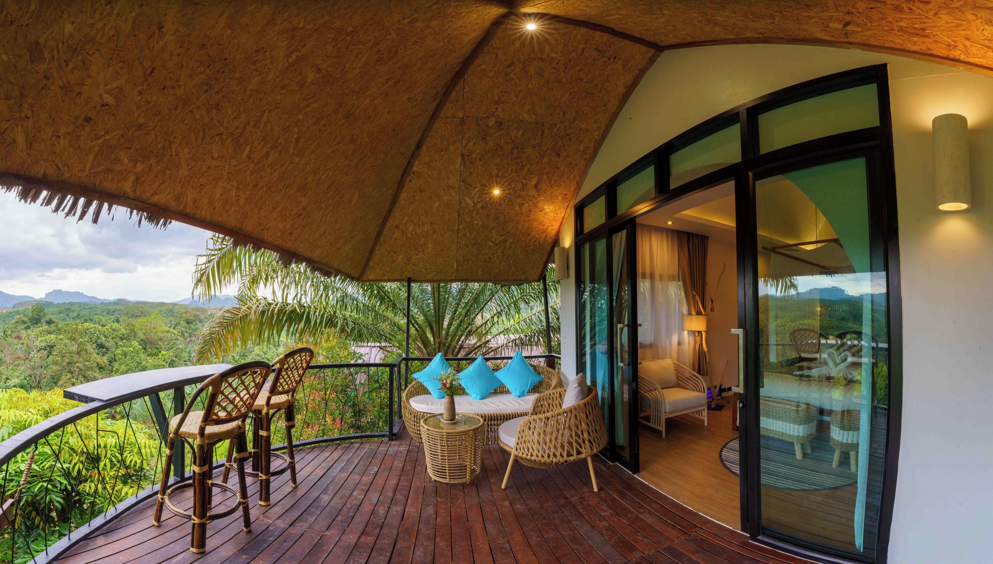A balcony with wicker furniture, a thatched roof, and a view of a lush landscape.
