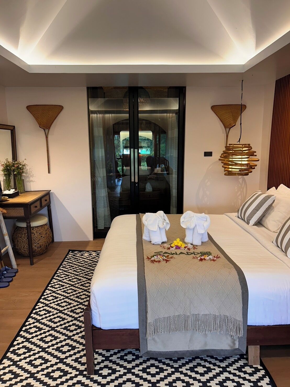 A hotel room with a bed, a desk, a chair, a mirror, and a view through a glass door.