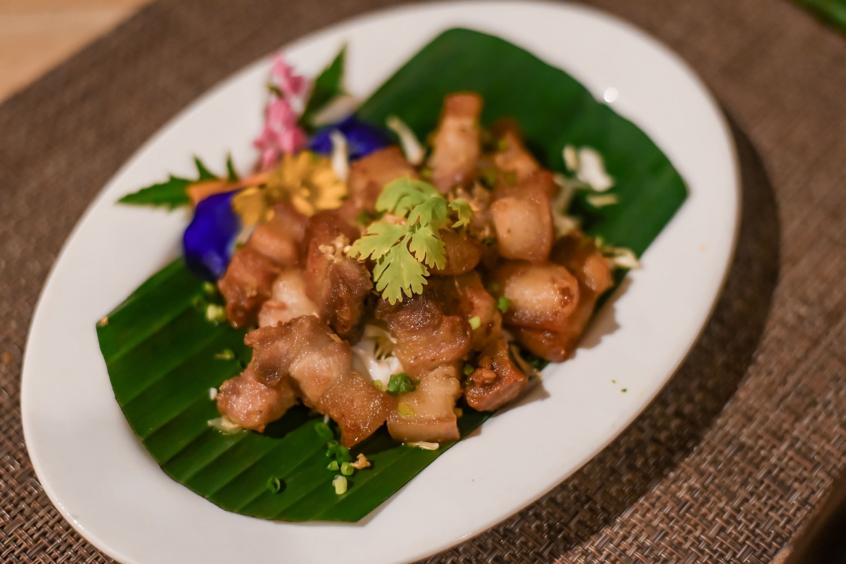A plate of food with pieces of meat and garnishes on a banana leaf.