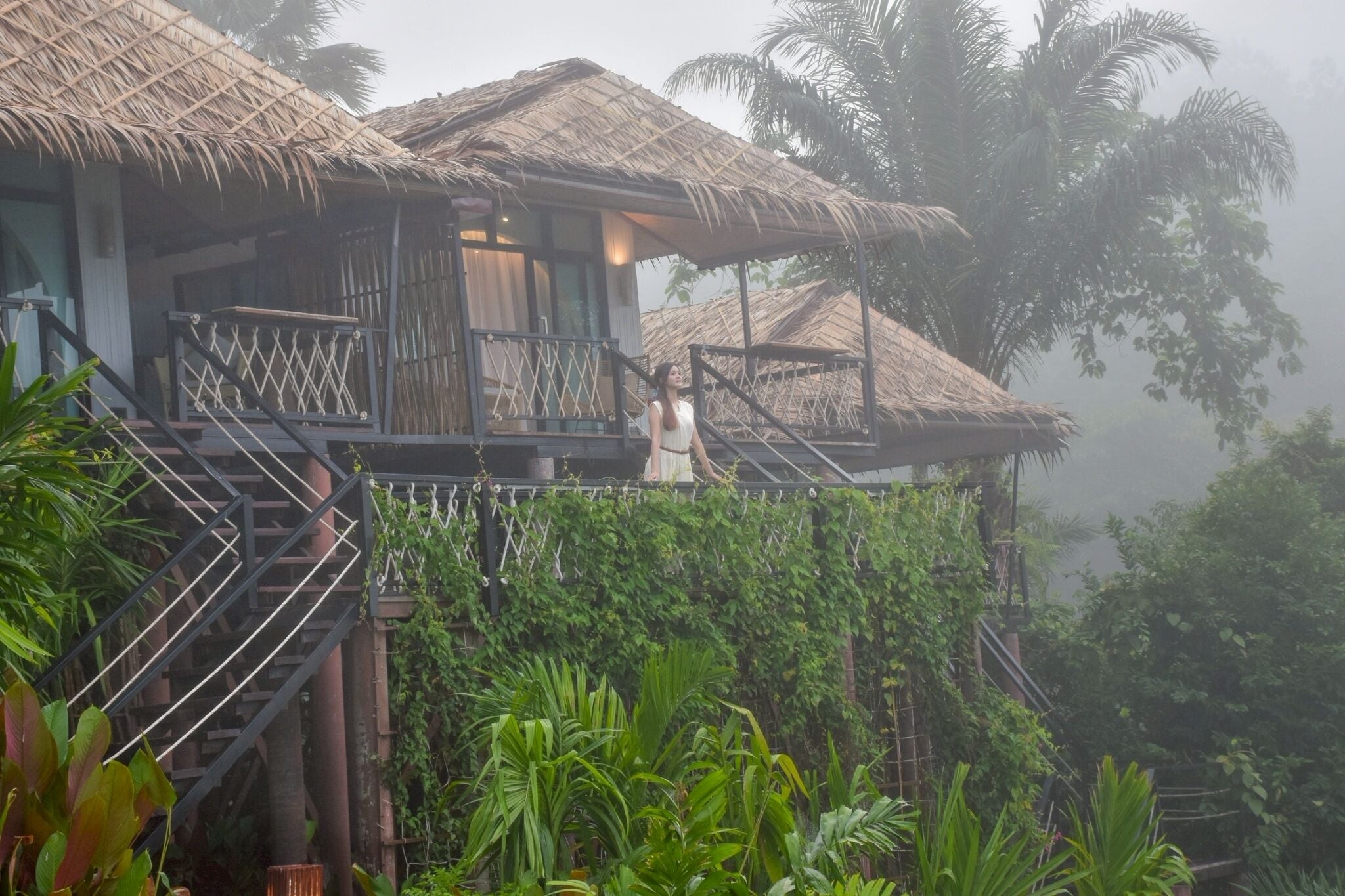 Un bungalow doté d’un toit de chaume, d’un balcon et d’une végétation luxuriante.