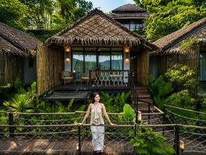 A thatched-roof structure with a balcony, surrounded by lush greenery.