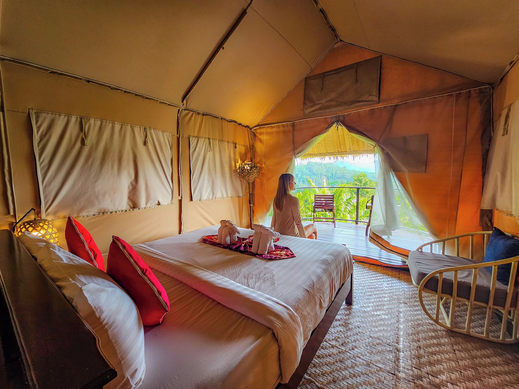 A tented accommodation with a bed, pillows, a chair, and a balcony with a view.