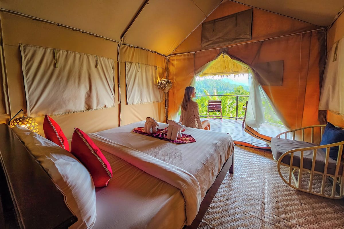 A tented accommodation with a bed, pillows, a chair, and a balcony with a view.