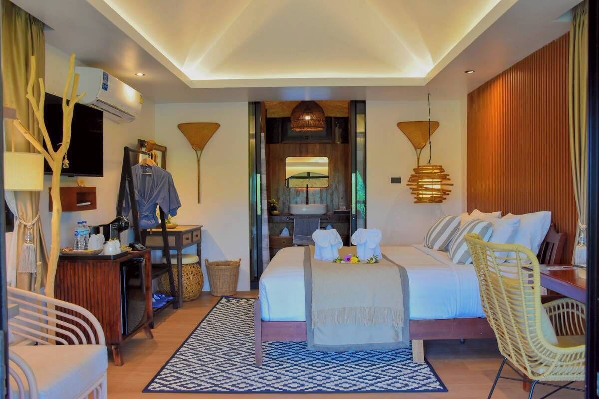 Habitación de hotel con cama, escritorio, silla, televisión y baño visible a través de una puerta abierta.