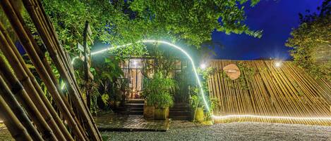 Un'area giardino all'aperto con un arco in bambù, gradini che conducono a un edificio e una recinzione in legno.