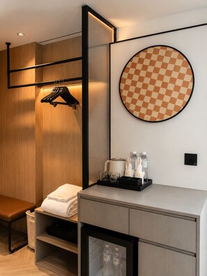 A modern hotel room with a built-in wardrobe, a round mirror, a bench, and a small table with toiletries. - L-Seven Hotel (Bangkok)