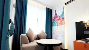 Habitación de hotel con sofá, una mesa redonda, televisor montado en la pared y un adorno mural.