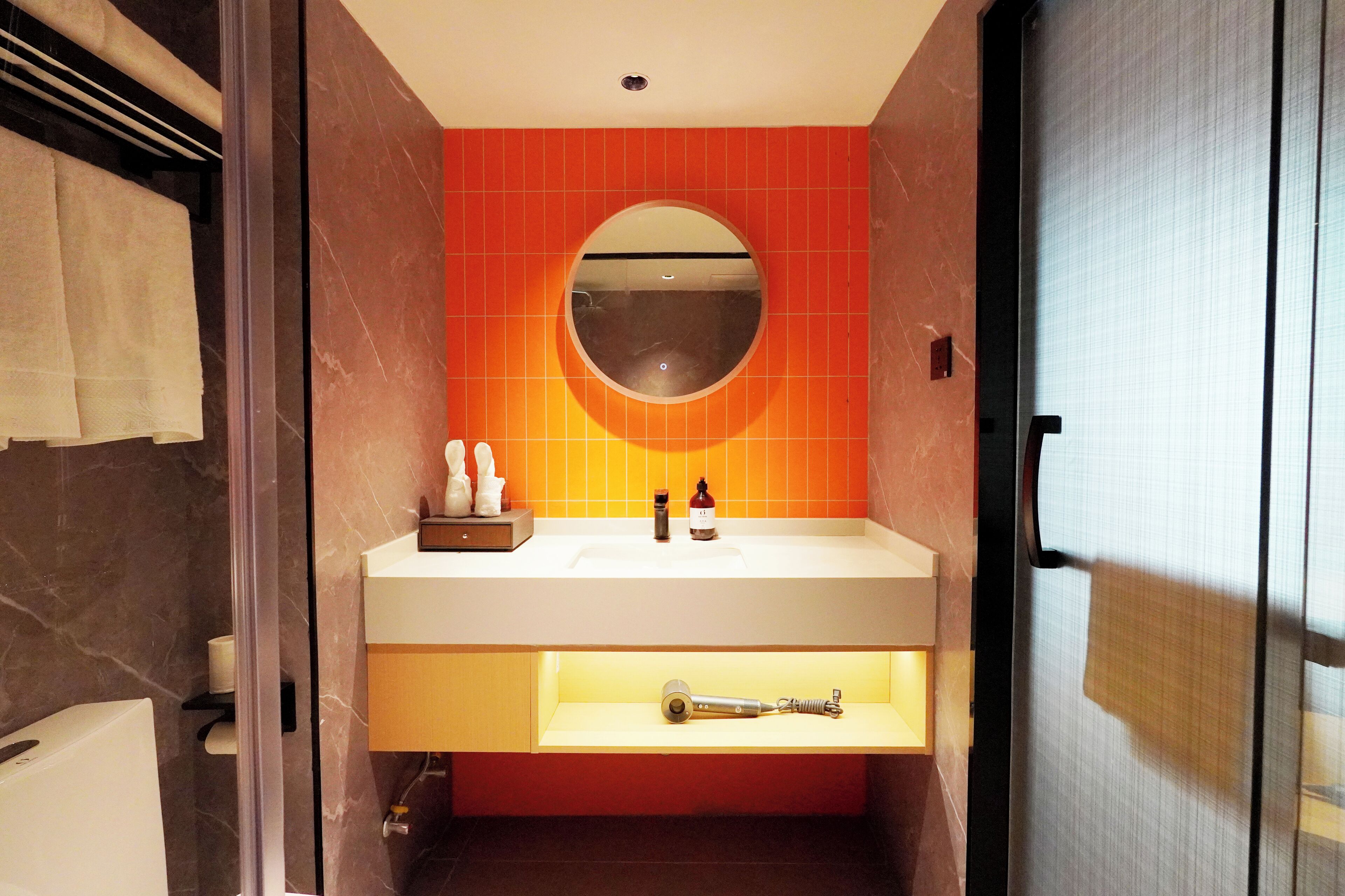 A bathroom with a white sink, a round mirror, and orange tiles.