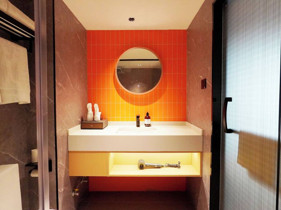A bathroom with a white sink, a round mirror, and orange tiles.