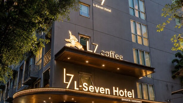 Exterior del hotel L-Seven, con señalización iluminada, una entrada destacada y una cafetería en la planta baja.