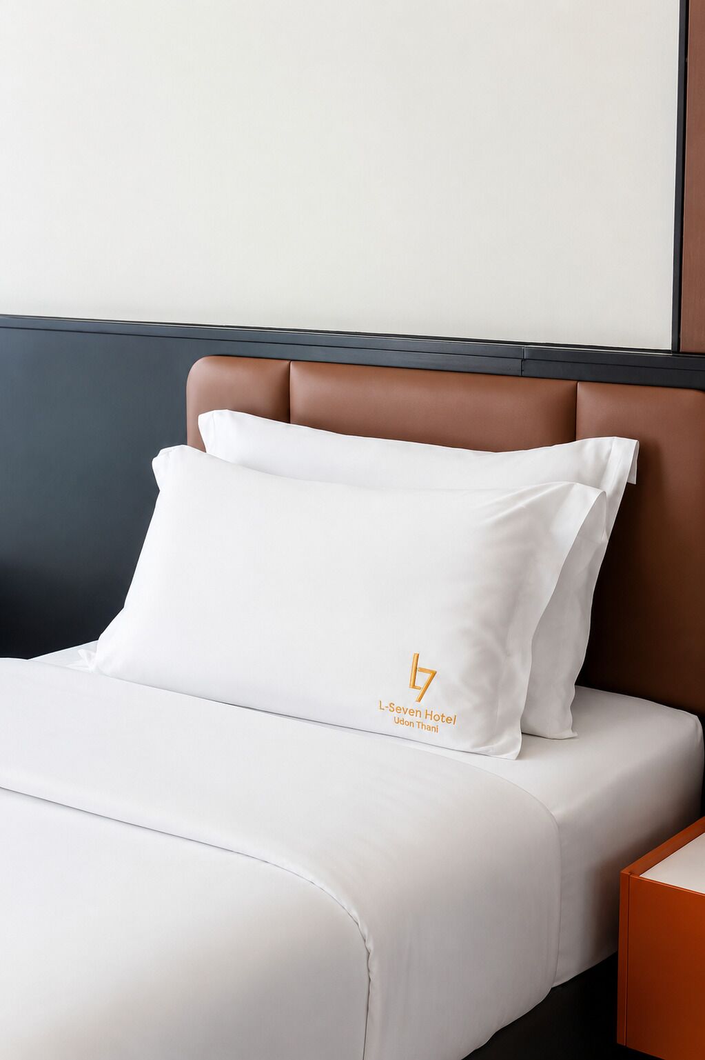 A hotel room with a bed, a pillow with a logo, and a nightstand.