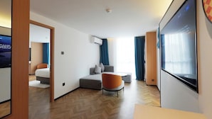 Una habitación de hotel moderna con sofá, sillón y una pantalla de televisión grande.