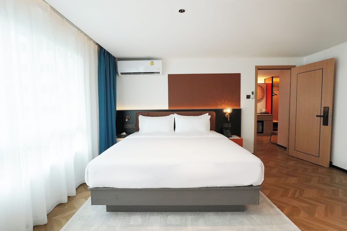 Una habitación de hotel moderna con una cama grande, un cabecero de madera, aire acondicionado de pared y vistas al baño.