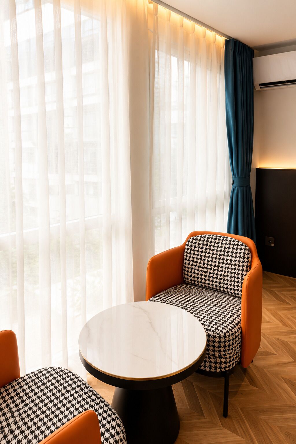 A modern room with a round table, two orange armchairs, and a patterned sofa.
