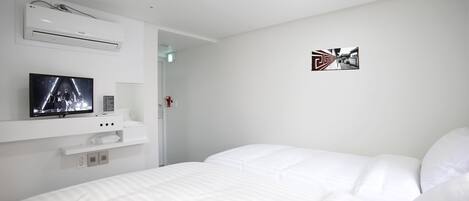 A hotel room with a bed, a TV, an air conditioner, and a door.