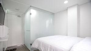 A modern hotel room with a large bed, a glass shower enclosure, and a white wardrobe.