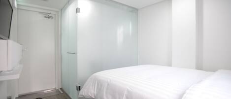 A modern hotel room with a large bed, a glass shower enclosure, and a white wardrobe.