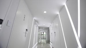A modern, well-lit hallway with white walls, recessed lighting, and a glass door at the end.