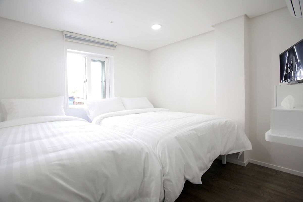 Un dormitorio con dos camas, una ventana y un televisor montado.