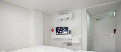A hotel room with a bed, a mounted TV, an air conditioning unit, and a door.