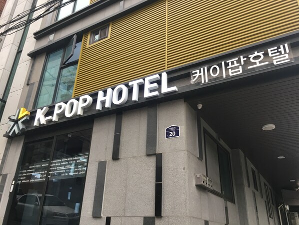 The exterior of K-Pop Hotel with a modern facade, large windows, and a prominent sign.