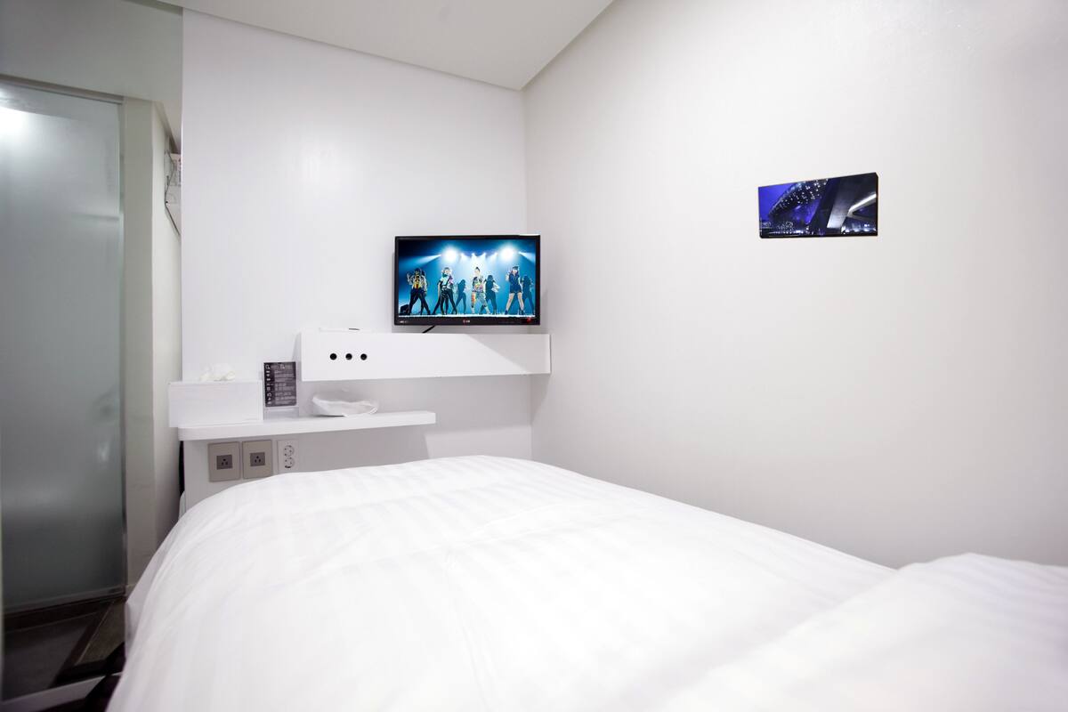 Habitación de hotel con cama, televisor montado en la pared y una mesita con teléfono y control remoto.