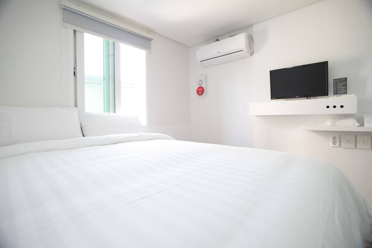 Habitación de hotel con cama, televisor montado, equipo de aire acondicionado y ventana con vistas.