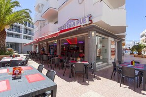 Un espace extérieur aménagé avec des tables et des chaises, une enseigne indiquant « SAFFETERIA PUET », et un bâtiment en arrière-plan.