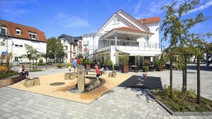 An outdoor public square with a fountain, seating areas, and a café. - Limes Hotel (Wehrheim)