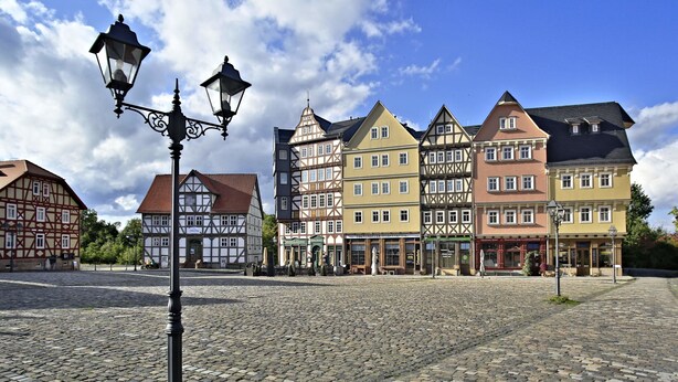 A cobblestone square with traditional half-timbered buildings, a black lamppost, and a clear blue sky. - Limes Hotel (Wehrheim)