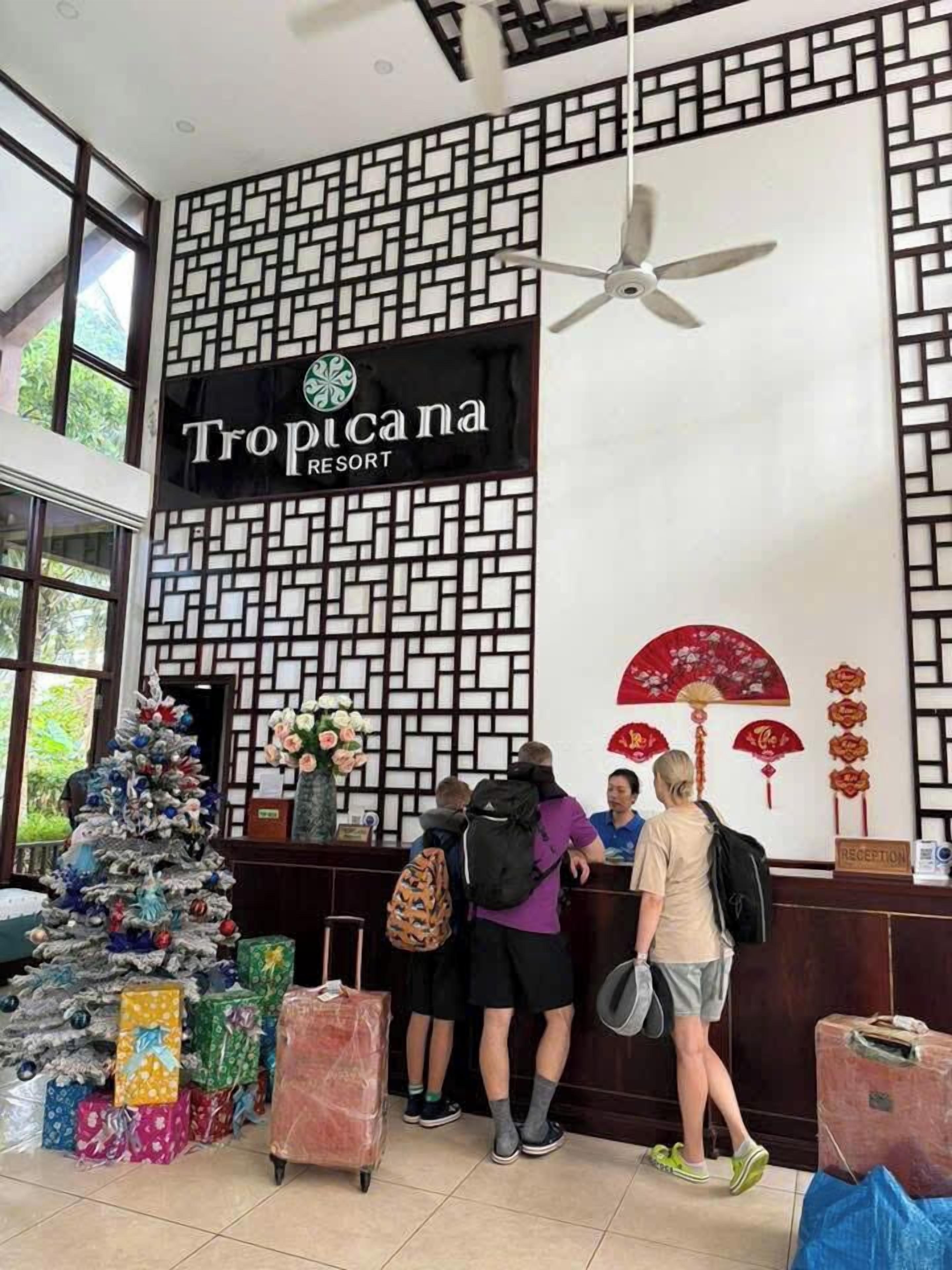 A Tropicana Resort reception desk with a decorative wall, a Christmas tree, and guests with luggage.