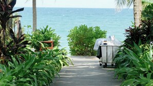 A paved pathway leading to a beach with palm trees and a covered grill. - Tropicana Resort (Phu Quoc)