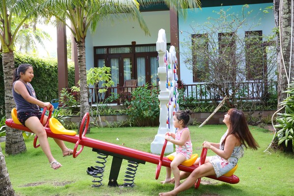 A seesaw with two children and an adult in a garden setting.