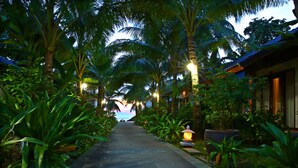A pathway lined with palm trees and a building with a tiled roof. - Tropicana Resort (Phu Quoc)