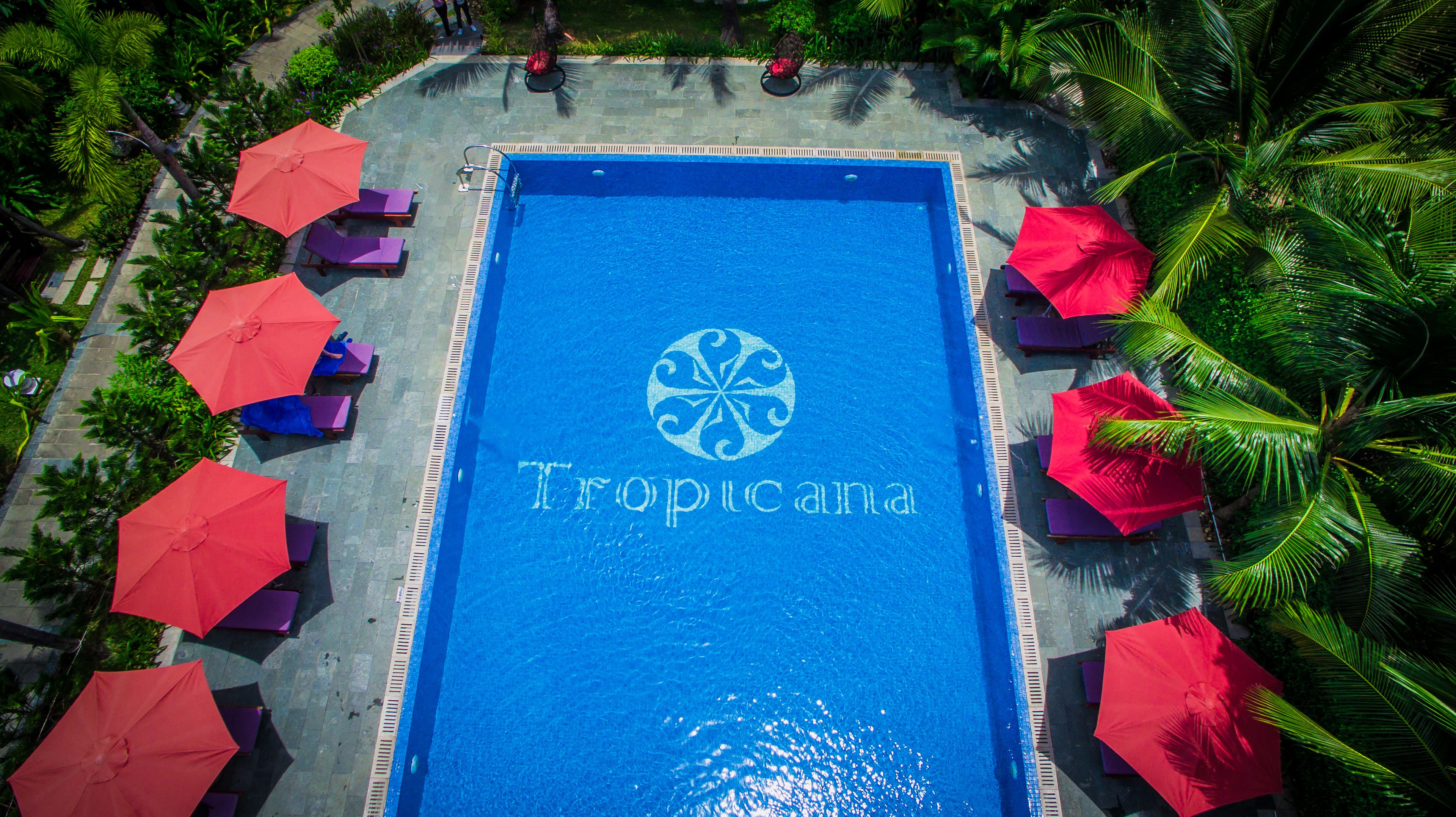 A swimming pool with the Tropicana logo, surrounded by palm trees and red umbrellas.