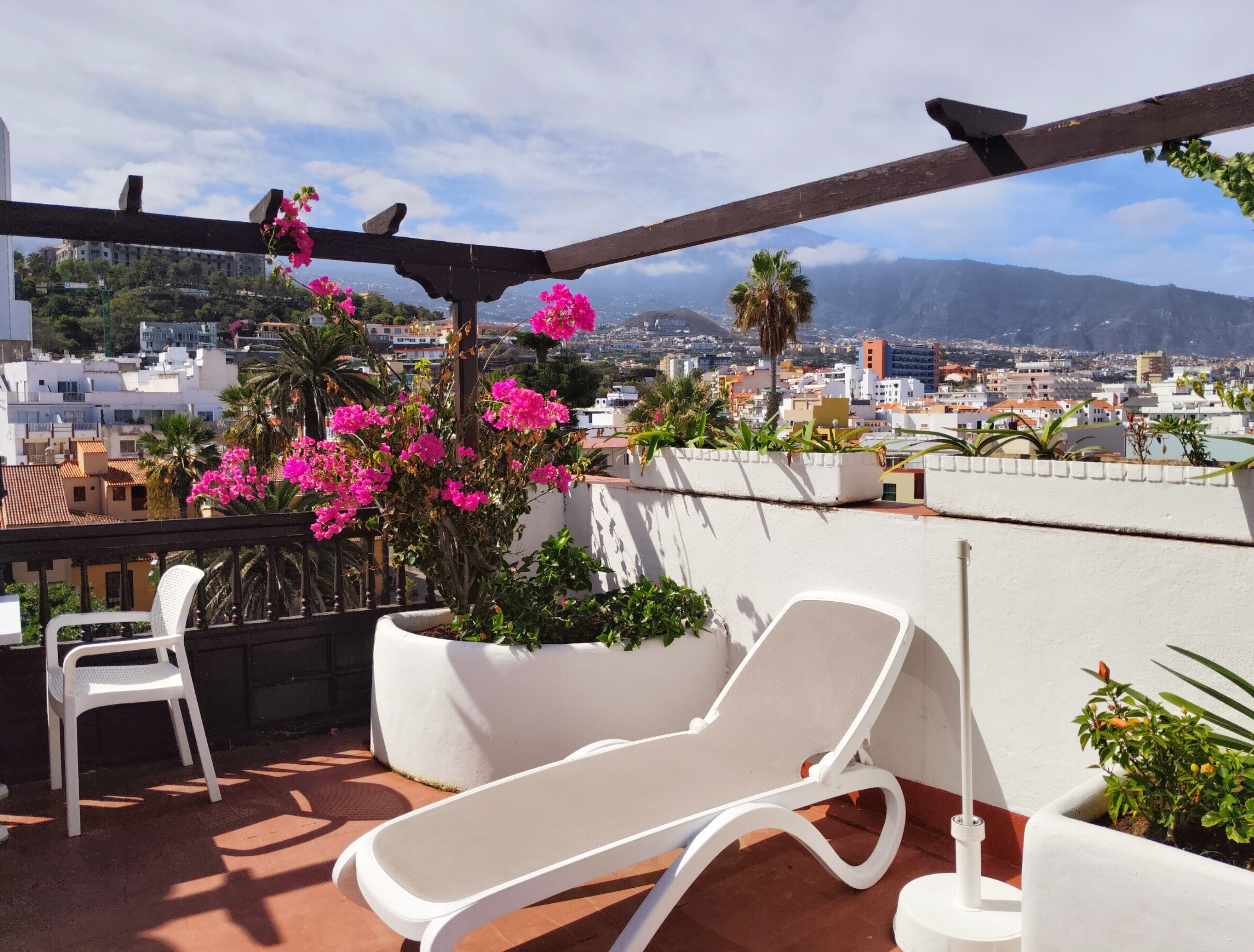 Una terraza en la azotea con una silla de descanso blanca, una silla blanca y una pérgola con flores rosas.