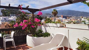 Una terraza en la azotea con una silla de descanso blanca, una silla blanca y una pérgola con flores rosas.