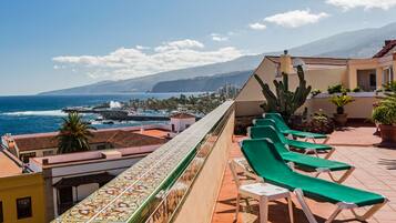 A rooftop terrace with green lounge chairs, a view of the ocean, and a tiled floor.