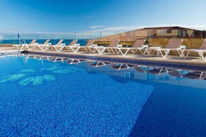 Una piscina con sillones de descanso y vistas al océano.