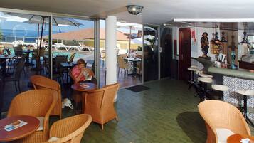 Un restaurante con mobiliario de mimbre, vista a la piscina y zona de bar.