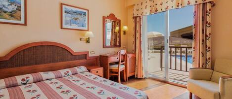 Habitación de hotel con cama, escritorio, silla, espejo y vista a una piscina.