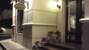 Entrada de um edifício com uma placa indicando "AURUM" e uma pequena área externa com mesas e vasos de flores.