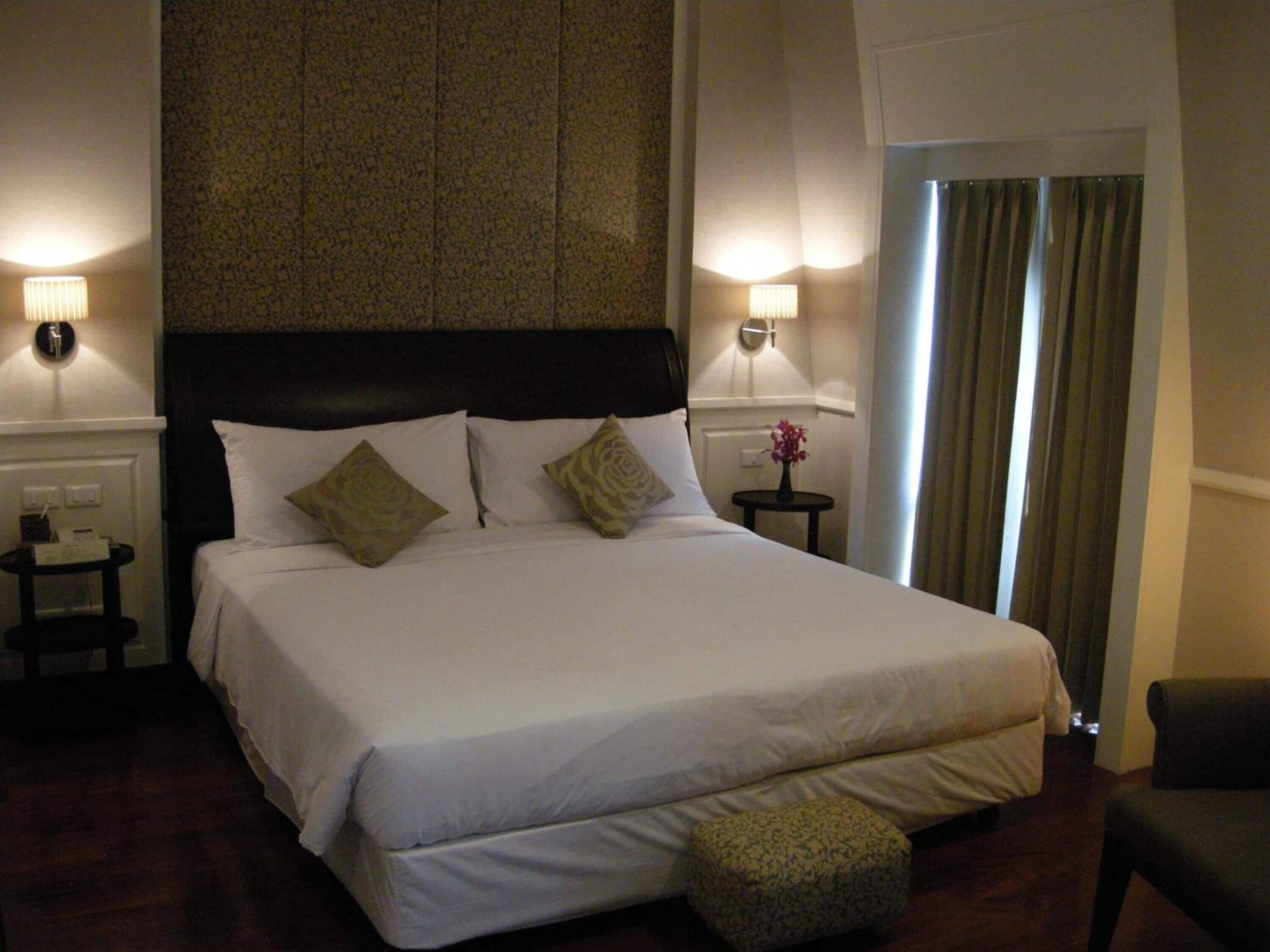 A hotel room with a large bed, two bedside tables, a chair, and a view of the outside through a window with curtains.