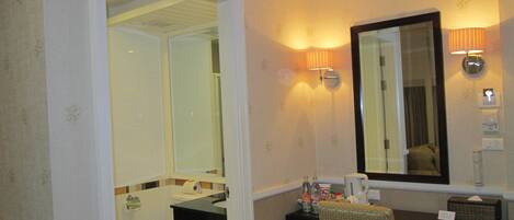 A bathroom with a toilet, sink, and mirror. There is a chair and a small table with toiletries.