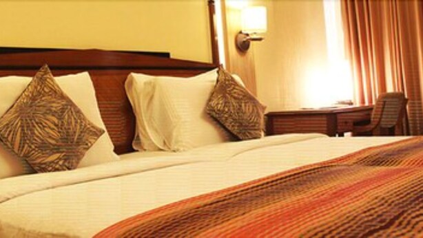 A hotel room with a large bed, two pillows, a bedside table with a lamp, and a chair. - Hiltop Hotel (Mumbai)