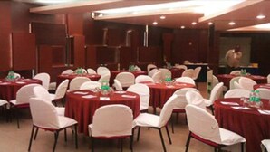 A conference room with multiple round tables, white chairs, and red tablecloths. - Hiltop Hotel (Mumbai)