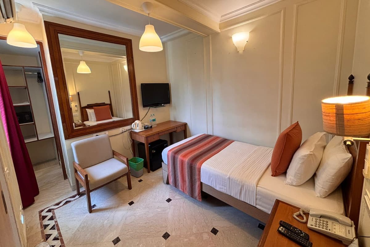 A hotel room with a bed, a desk, a chair, a TV, a lamp, and a telephone.